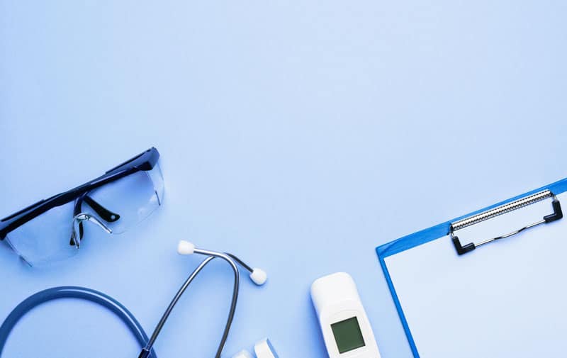 Schutzbrille, Stethoskop, Fieberthermometer und Klemmbrett auf blauem Hintergrund, wir unterstützen das Gesundheitswesen mit Schädlingsbekämpfung und Hygienemanagement